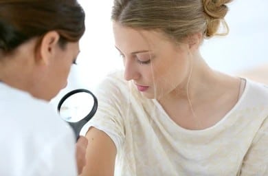 A dermatologist examining a mole on a woman's arm